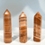 Three Red Banded Calcite towers positioned upright, standing side-by-side. The polished mineral pieces have a six-sided, hexagonal shape and come to a sharp point, displaying striking natural horizontal layers of orange-brown, tan, and white. Three Red Banded Calcite towers positioned upright, standing side-by-side. The polished mineral pieces have a six-sided, hexagonal shape and come to a sharp point, displaying striking natural horizontal layers of orange-brown, tan, and white.