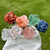 Outdoor display of colorful Forever Rose arrangements featuring pink, blue, red, green and iridescent rose blooms on white cloth.