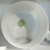Top-down view into the interior of a white frosted crystal singing bowl. At the center of the bottom is a green circular emblem featuring the Heart Chakra symbol (Anahata) and the letter "F," indicating its musical note.