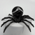 A close-up view of a sardonyx gemstone spider resting on a white stand. The focus is on the intricate white orb-like banding of the black gemstone and the textured detail where the metal legs join the stone body.