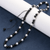 An adjustable 6mm black obsidian and pearl necklace draped over a white cylindrical display stand against a dark blue background. The shot emphasizes the delicate size of the 6mm gemstone beads and the high-contrast, elegant aesthetic of the piece.