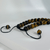 A close-up, angled view of a beaded necklace featuring 12mm polished Tiger Eye gemstones. The stones show characteristic chatoyancy with shimmering bands of golden yellow, honey brown, and deep black. The necklace is strung on a black cord with an adjustable sliding knot closure, finished with two smaller Tiger's Eye beads at the ends of the pull-strings.