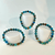 Three beaded stretch bracelets crafted from round, polished natural blue kyanite gemstones, displayed on staggered white cylindrical risers against a white background. The gemstone beads showcase a striking gradient of deep indigo, bright denim, and translucent white-blue mineral patterns, highlighting the unique textures and reflective sheen across multiple pieces.