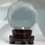 Clear crystal ball on a polished dark brown wooden base, illuminated from below, with a softly blurred light gradient background.