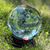 Large crystal ball on a black display stand reflecting an inverted outdoor sky and garden landscape.