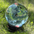 Large crystal ball on a black display stand reflecting an inverted outdoor sky and garden landscape.