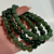 Stack of natural green Jade gemstone stretch bracelets featuring smooth polished beads held in hand.