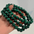 Stack of polished Malachite gemstone stretch bracelets featuring vibrant green beads with distinctive natural swirling patterns held in hand.