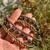 Hand holding elastic copper bead bracelets in gold, rose gold, and dark hematite against blurred green foliage.