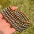 Stack of silver and gold stainless steel stretch bead bracelets against a natural green background.