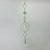 Hanging gold-tone sun catcher with three diamond-shaped frames, lavender beads, and faceted iridescent crystals against a blurred green lawn.