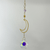 Gold crescent-moon suncatcher with a lavender amethyst stone, sunburst charm, and faceted rainbow-reflective crystal.