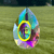 Faceted, multicolored teardrop sun catcher with a yellow-rimmed central oval, hanging against a blurred green lawn.