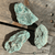 Rough Fuchsite green mineral specimens displayed on a rustic wooden surface, showcasing their natural pale green color and textured crystalline patterns.