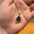 Close-up of a rough Moldavite necklace held in hand, highlighting the genuine raw green Moldavite gemstone and sterling silver pendant setting.