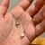 A hand holding two teardrop necklaces made of silver chain, each with a shimmering rainbow moonstone pendant.