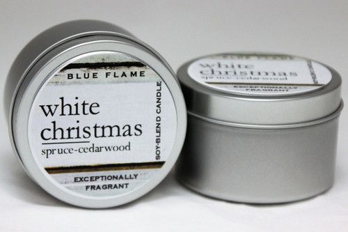 There are two silver, modern designed travel tins in the image. One tin is on it's side to show what the top of the label looks like on the lid: It says, white christmas underlined in the middle of the label, and is off set towards the left side in large text, spruce-cedarwood are written below in a smaller font. The Blue Flame logo is at the top of the label. Soy-blend Candle is written on the right side in a vertical line. On the bottom of the label is written, Exceptionally Fragrant. The other tin is flat and shows that the tin is just silver without a wrap around label. The modern design uses pale hues and simplistic lines.