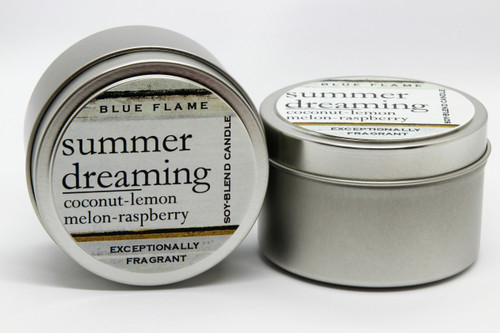 There are two silver, modern designed travel tins in the image. One tin is on it's side to show what the top of the label looks like on the lid: It says, summer dreaming underlined in the middle of the label, and is off set towards the left side in large text, coconut-vanilla-melon-raspberry-lemon are written below in a smaller font. The Blue Flame logo is at the top of the label. Soy-blend Candle is written on the right side in a vertical line. On the bottom of the label is written, Exceptionally Fragrant. The other tin is flat and shows that the tin is just silver without a wrap around label. The modern design uses pale hues and simplistic lines.