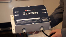 Person holding a BarnTalk gateway with a blue faceplate and power cable connected