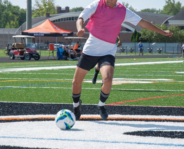 Male player in pink scrimmage vest dribbling affordable soccer ball on turf field