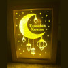 An Islamic art painting of Ramadan in a wooden frame, illuminated with Yellow lighting that runs on a battery