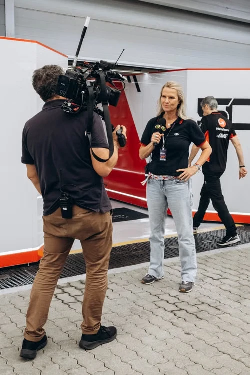 An operator with a shouldered, wirelessly-rigged camera filming an interview subject at eye height in a paddock.