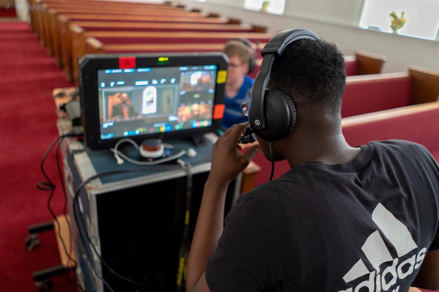 A volunteer operator in a headset working a multi-camera switcher at the back of a church auditorium.