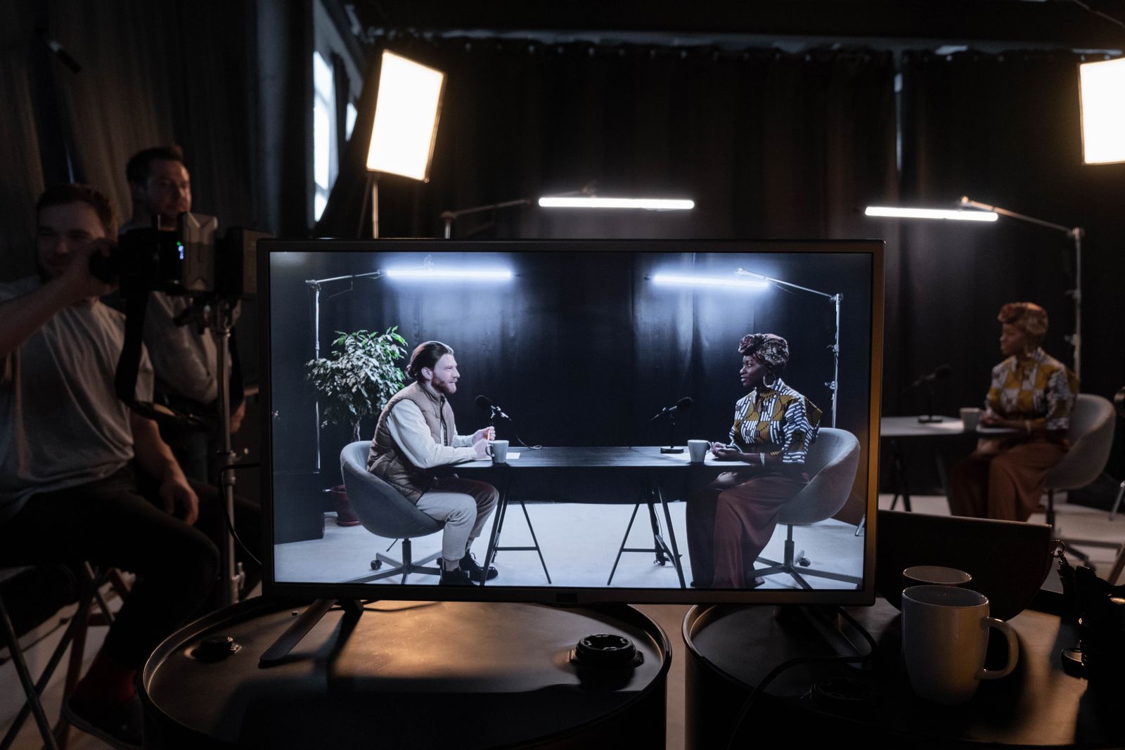 A studio set with lighting and crew, and a monitor showing the programme being recorded.