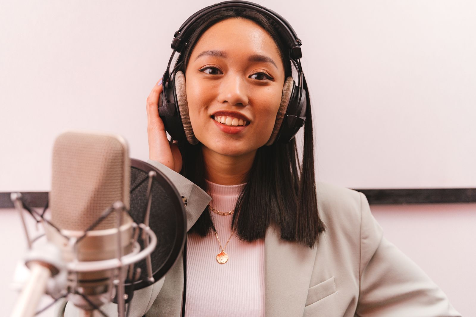 A presenter in headphones speaking straight to camera into a studio microphone.