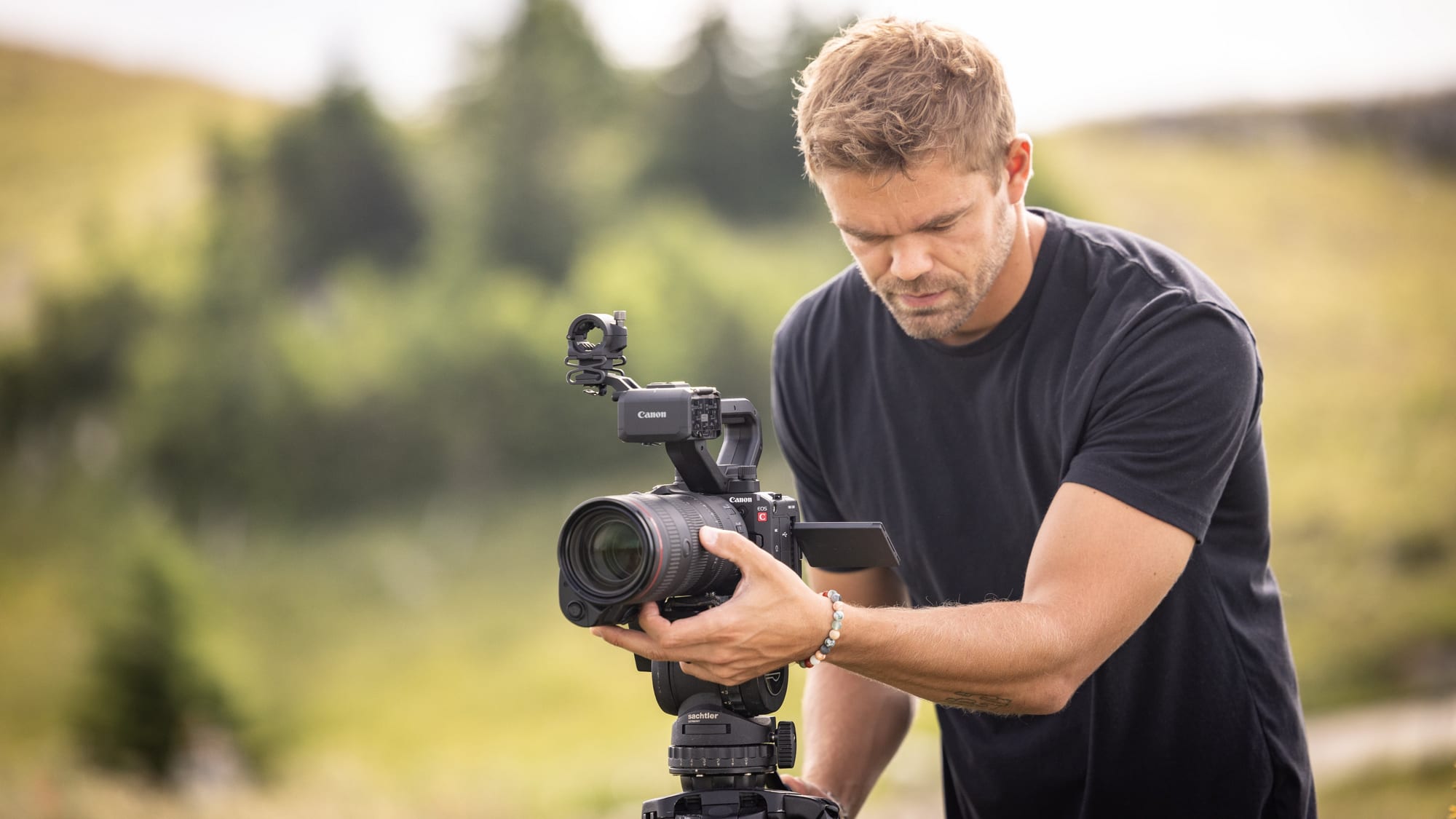 A solo operator with a compact Canon cinema camera on a tripod, shooting on location in natural light.