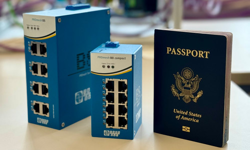 The B8 Compact managed switch is sitting on a desk in between two larger objects for size. To the right of the B8 Compact is a passport that is slightly taller than the B8 Compact. To the left of the B8 Compact is a regular-sized B8 switch and it is twice the size of the B8 Compact.