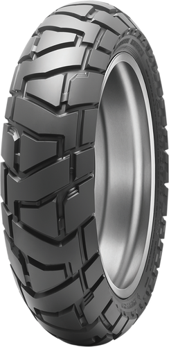 A studio product photograph of the Dunlop Trailmax Mission rear motorcycle tire in 140/80B18 70T sizing, set against a clean white background. Mounted on a metallic silver rim and standing vertically at a three-quarter perspective, the tire showcases its heavy-duty 50/50 dual-sport adventure tread profile engineered for medium-to-large capacity adventure and dual-sport motorcycles. It features aggressive, deep-grooved tread blocks with staggered step-down lugs designed to maximize off-road traction across dirt, gravel, and rocky terrain while ensuring exceptional stability, noise reduction, and high mileage on paved roads, completed by distinct wrap-around shoulder lugs and embossed "TRAILMAX MISSION" branding along its durable matte black bias-belted construction.