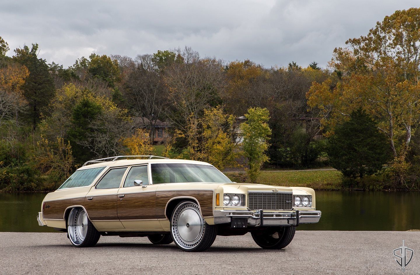 Cream Chevrolet station wagon with woodgrain sides on large polished wheels, parked by a lake in autumn
