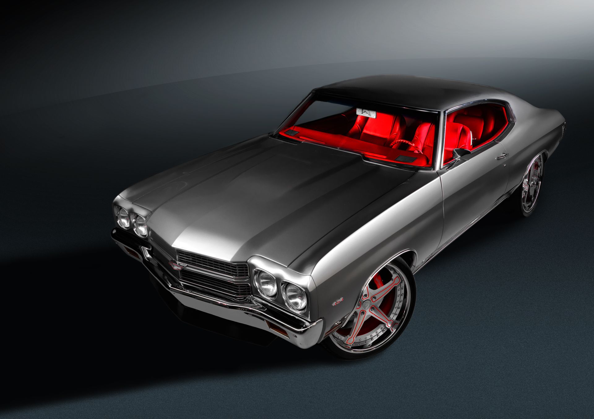 Silver Chevelle with red interior and red-accented polished custom wheels in a dark studio
