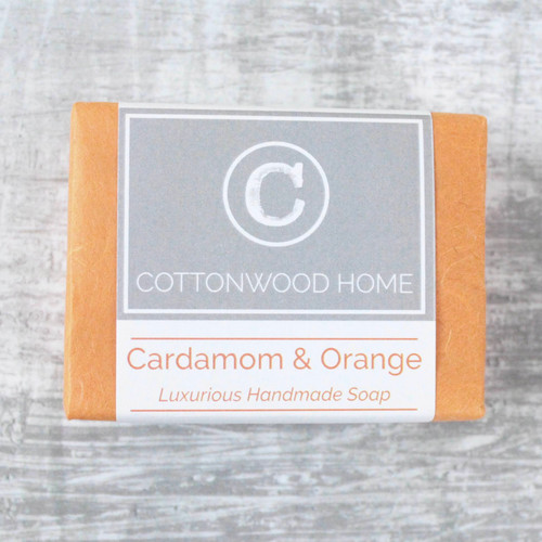 A bar of cardamom and Orange soap wrapped in orange tissue with a printed branding and info band