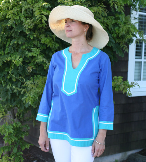 Woman wearing a hat and a cobalt blue tunic with contrasting teal and white trim.



