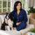 Woman sitting on couch with Border Collie and wearing solid navy cotton two-piece pajama set with white trim.