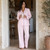 Woman wearing long sleeve pink and white seersucker pajamas with navy blue piping standing in doorway.