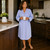 Woman wearing cotton button-down blue and white striped seersucker long sleeve nightshirt with pink piping, standing in kitchen with cup in her hand
