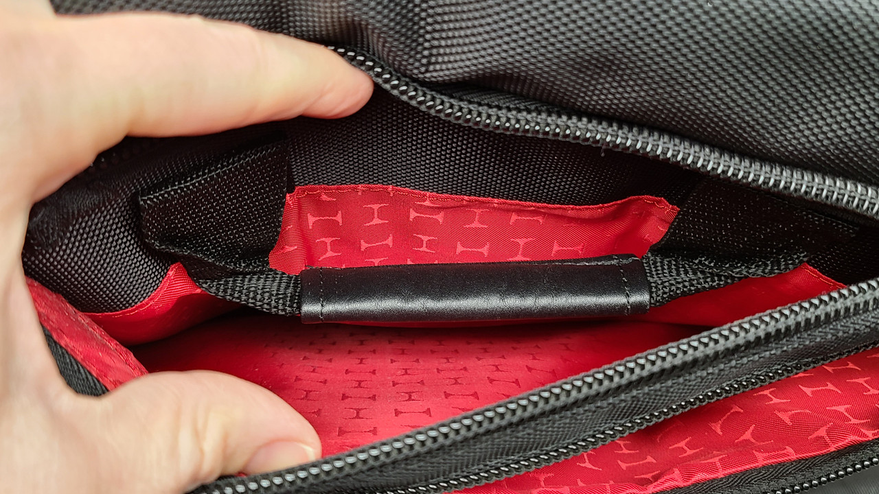 Small zipper on the top of the backside of the bag holds a single hidden handle