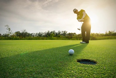 Close up view of a golf ball rolling toward a hole with a golfer in the background