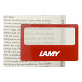 A red pocket ruler magnifier with a clear lens, placed over text in a book, featuring a logo.