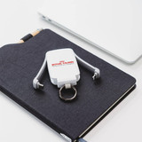 A white mini power bank with a keyring, placed on a dark notepad beside a silver laptop. It has a logo on it.