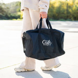 A person carrying a navy RPET duffle bag with handles and a shoulder strap. The bag features a logo.