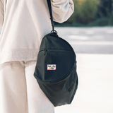 A black duffle bag with a logo, featuring a shoulder strap and zippered pocket, held by a person in light-coloured clothing.