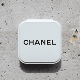 A compact mirror in a white case with a logo on the top, set against a textured stone background.