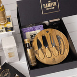 A gourmet gift pack featuring a bamboo cheese board set, assorted snacks, and a selection of condiments in a black box.