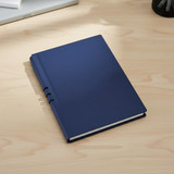 A navy blue hardcover notebook with a textured cover, resting on a wooden desk. It features a logo on the front.