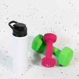 A drink bottle in white with a black lid, beside a pair of pink and green dumbbells on a speckled surface.