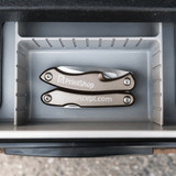 A silver multi-tool featuring several tools, placed inside a grey storage compartment. The tool has a branded logo.